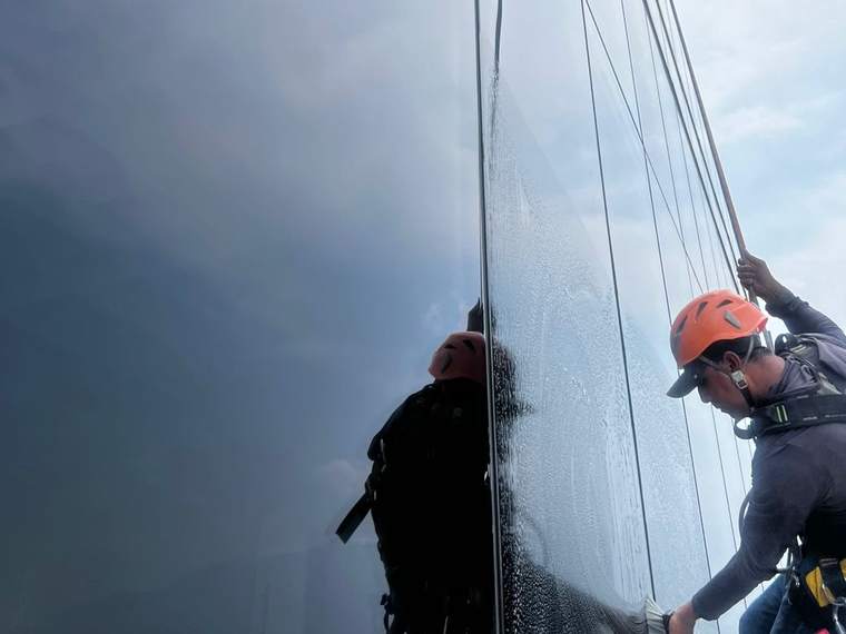 Técnico con casco y arnés lavando cristal con cepillo en fachada